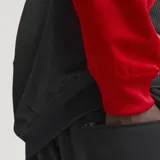 Campera deportiva Adidas SST de corte holgado, confeccionada en tejido de malla color negro con mangas rojas y detalles de franjas blancas características de la marca. Cuenta con cuello tipo bomber, cierre frontal completo y logo del trifolio bordado en el pecho.