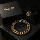 Pulsera de eslabones tipo cubana en acero con baño de oro, destacada por un cierre central con diseño de flor de lis en tono plateado.