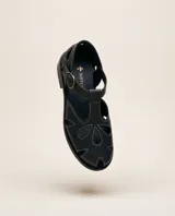 Sandalias de cuero negro con calados orgánicos y costuras en contraste color blanco, pulsera regulable con hebilla y taco bajo.