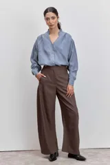 Camisa de satén color azul grisáceo, con cuello mao con detalle de volados, cierre frontal con botones y mangas largas con puños abotonados.