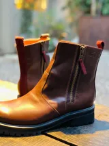 Botas de cuero marrón, con doble cierre lateral con tiradores de gamuza bordó, suela gruesa de goma y tira trasera para facilitar el calce.