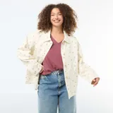 Sobrecamisa de twill color blanco con estampado floreado sutil, corte holgado, cuello camisero, cierre frontal con botones metálicos y dos bolsillos de parche delanteros.