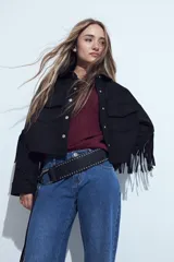 Campera negra de estilo western con flecos en las mangas, corte cropped, bolsillos frontales y cierre con botones metálicos.