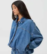 Campera de jean azul estilo balloon, con cuello tradicional, cierre frontal oculto y bajo con elástico.