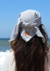 Conjunto compuesto por un pareo corto tipo falda cruzada con estampado de rayas verticales y una bandana a juego. El pareo cuenta con un lazo lateral para ajuste y un pequeño detalle bordado en el frente.