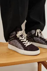 Zapatilla de caña media con paneles de gamuza bordó y laterales cubiertos de glitter plateado. Presenta detalles de tachas metálicas en la parte trasera, cordones blancos y suela de goma blanca.