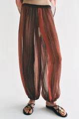 Pantalón semitransparente de tiro medio, corte bombacho con cintura y puños elásticos, con diseño de rayas verticales en tonos marrones y rojizos.
