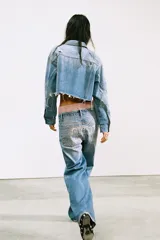 Jeans de denim azul claro, tiro medio, corte recto y holgado. Presenta cinco bolsillos y detalle de letras y brillos en la parte trasera.