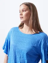 Blusa de mujer color azul vibrante con textura acanalada y pequeños patrones jacquard en relieve. Presenta un escote redondo y mangas cortas con vuelo.
