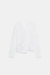 Camisa blanca de popelín con cuello solapa y escote en pico. Presenta manga larga y un detalle de tejido drapeado en el delantero, con cierre frontal cruzado.