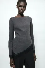 Top de manga larga en tejido de punto suave color gris, con cuello redondo y bajo asimétrico decorado con encaje negro a tono. Presenta detalles de encaje negro en los puños.