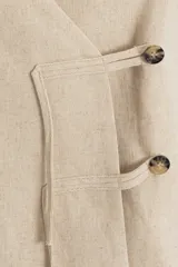 Chaleco de lino con escote en V profundo y cierre frontal cruzado mediante dos botones y tiras de ajuste. Diseño sin mangas y corte recto.