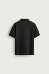 Remera polo regular fit de color gris oscuro, confeccionada en tejido de algodón con textura de rayas verticales. Cuenta con cuello solapa, cierre frontal con botones y mangas cortas con terminación en rib.