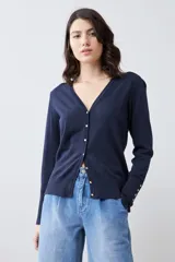 Cardigan de punto negro con escote en V, cierre frontal con botones metálicos dorados y mangas largas con puños ajustados que incluyen detalles de botones decorativos.