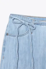 Pantalón de jean estilo pijamero de tiro medio, con cintura elástica ajustable mediante cordones. Presenta corte recto, bolsillos laterales y cierre frontal con cremallera y gancho metálico.