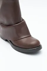 Bota de caña baja color negro, confeccionada en poliuretano con acabado liso y estructura flexible que genera un efecto fruncido. Presenta puntera redondeada, base baja y un cierre metálico en la parte trasera de la caña.
