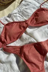 Conjunto de bikini rosado con acabado brillante, compuesto por un top con tirantes y contorno regulables y copas removibles, y una bombacha colales.