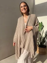 Ruana tejida en punto jersey, color negro con destellos brillantes de lurex. Presenta una etiqueta de cuero sintético con logo en la parte posterior.