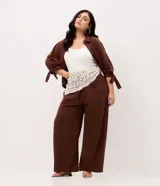 Pantalón palazzo marrón de talle alto y pierna ancha, confeccionado en sarga de algodón y liocel, con cintura elástica y bolsillos laterales.