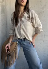 Camisa beige de manga larga con cuello en V, cierre frontal de botones y delicados bordados florales en marrón en la zona del pecho y en los puños.