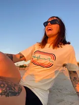 Remera color crema de algodón con estampa en la espalda de un paisaje playero con el texto "Chema Sure Chate et la mer".