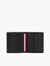 Billetera trifold de cuero vacuno color negro con textura acanalada y logo de Tommy Hilfiger en la parte inferior. Cuenta con múltiples ranuras para tarjetas, compartimento para billetes y bolsillo interior con cierre a presión para monedas.