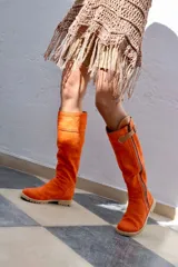 Botas altas color naranja de gamuza forradas en cuero, con cierre lateral y hebilla decorativa.