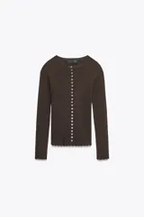 Chaqueta ajustada de punto acanalado color marrón oscuro, con cuello redondo y manga larga. Presenta un cierre frontal completo con botones pequeños y blancos. Los bordes del ruedo y los puños tienen un acabado festoneado.