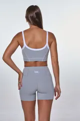 Conjunto deportivo compuesto por un top y un short de tiro alto en color gris. El top presenta breteles blancos, escote redondo y el logo de la marca estampado en el frente. El short cuenta con costuras decorativas blancas que realzan el diseño.