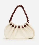 Cartera hobo marca Satinato en poliuretano color marfil, con diseño fruncido, cierre de cordón ajustable y asa rígida de esferas de madera.