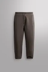 Pantalón jogger relaxed fit Zara Athleticz de tejido técnico compacto elástico con mezcla de algodón. Presenta cintura elástica ajustable con cordón, bolsillos laterales en la cadera, bolsillo trasero con cierre de cremallera, bajo ajustable con elástico y detalle de logo estampado en la pernera.