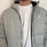 Campera inflada negra con capucha, cierre frontal blanco y puños elásticos acanalados. Presenta el logo de la marca Santa Barbara Outfitters bordado en el pecho.
