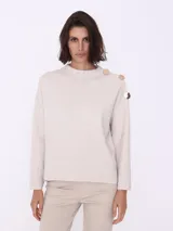 Sweater color beige de tejido de punto, con cuello redondo y mangas largas. Detalle de botones dorados en el hombro.