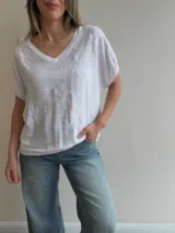 Blusa blanca de corte relajado, con escote en V, mangas cortas amplias y detalles de bordados florales en relieve.