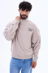 Buzo de felpa color beige con cuello alto, cierre frontal parcial y logo bordado en el pecho.