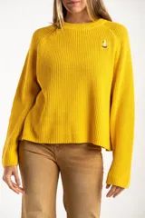 Sweater de punto en color amarillo, con diseño oversize, cuello redondo y manga larga. Presenta un pequeño bordado de un velero en la parte superior del pecho.