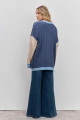 Cardigan de punto con diseño de bloques de color, combinando azul marino en el cuerpo y beige en las mangas. Presenta un tejido con textura de trenzas, cuello en V con borde rayado en azul y blanco, cierre frontal con botones y bolsillos delanteros. Incluye un parche decorativo en el pecho.