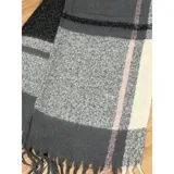 Bufanda rectangular de tejido grueso con diseño de cuadros en tonos gris, blanco y detalles en rosa. Presenta terminaciones con flecos en los extremos.