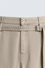 Pantalón de algodón color beige, estilo wide balloon fit, con cintura ajustable mediante cinturón de la misma tela. Presenta bolsillos frontales y bolsillos traseros de plastrón, con efecto lavado y abertura en el bajo.