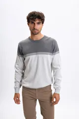 Buzo de punto con diseño de bloques de color en tonos gris oscuro y gris claro, separado por finas franjas horizontales. Presenta cuello redondo y puños acanalados.