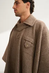 Poncho unisex de lana fina color marrón claro con cuello, cartera con broches a presión y bolsillo ojal. Diseño exclusivo de Don Baez, hecho 100% en Uruguay.