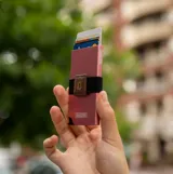 Billetera tipo tarjetero rígido de aluminio color rosa, con sistema deslizante automático para acceso rápido a tarjetas y protección RFID integrada.
