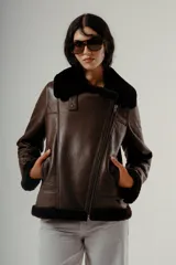 Chaqueta estilo aviador o biker de cuero marrón oscuro con forro y cuello de piel sintética negra. Presenta cierre asimétrico frontal y bolsillos laterales con cierre.