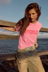 Remera de algodón color rosado con efecto lavado, de corte regular y cuello redondo, con texto rojo estampado en el frente que dice 'CENTER OF ATTENTION'.