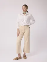 Pantalón jean color beige, de tiro alto y pierna ancha con terminación desflecada.