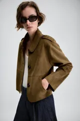 Chaqueta corta de efecto ante en color marrón, con cuello solapa, manga larga y trabillas en los hombros. Presenta cierre frontal con botones y bolsillos delanteros de doble vivo.