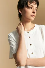Remera de manga corta color marrón, con cuello redondo y cierre frontal parcial con botones. Presenta un diseño de calce relajado y líneas simples.