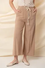 Pantalón ancho color beige, de hilo, con cintura elastizada ajustable con cordón y bolsillos laterales.