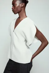 Top de Zara Woman Collection color blanco, con escote en pico, mangas cortas abullonadas con aberturas y cierre frontal con cremallera.