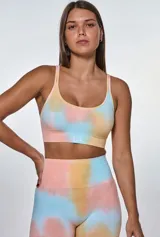 Conjunto deportivo compuesto por un top de escote redondo y un short de tiro alto, ambos con diseño tie-dye en tonos pastel salmón, amarillo y celeste. El top presenta el logo de la marca estampado en el frente.